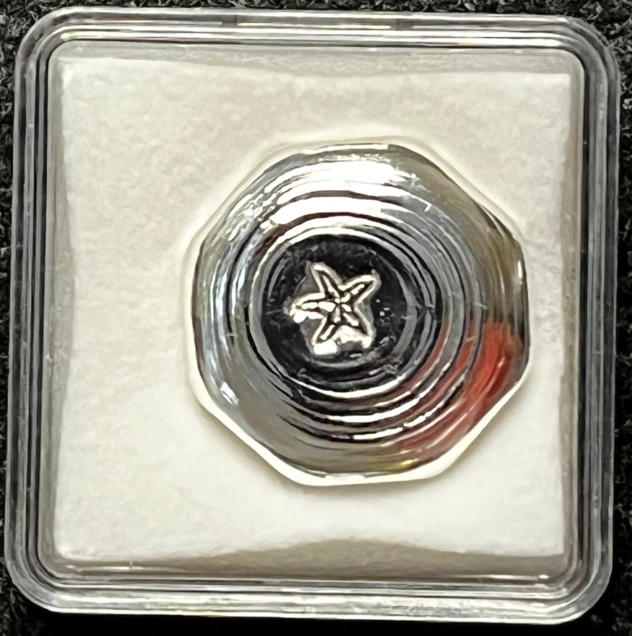 Silver coin with star design in a clear protective case on a dark textured background