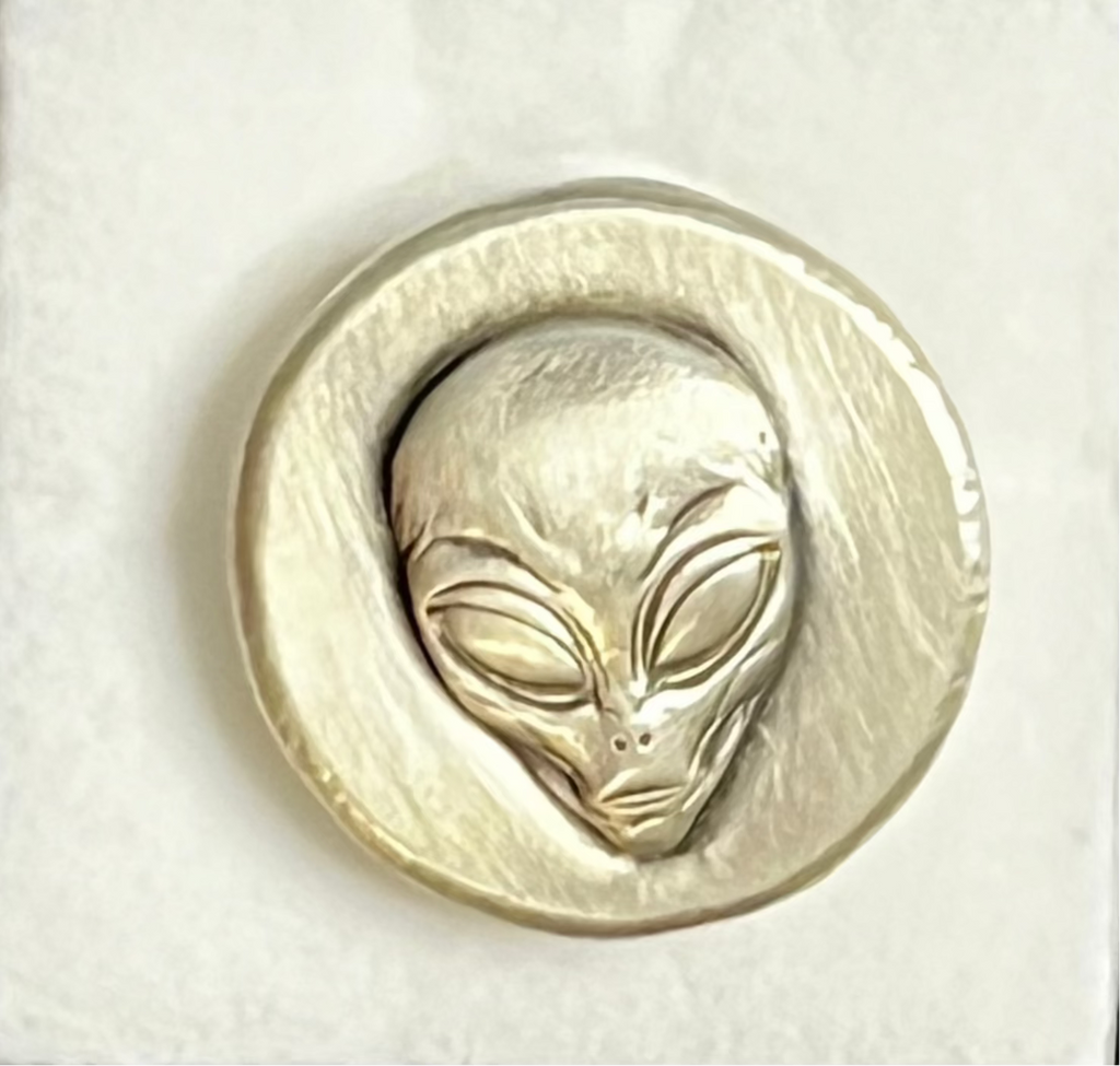Silver coin with a face design in a protective case on a dark textured background